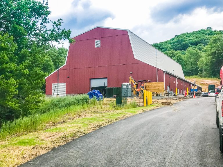 Red barn-style building with construction activity, surrounded by green trees and rolling hills, representing A3 USA's industrial or agricultural facilities, showcasing infrastructure development.
